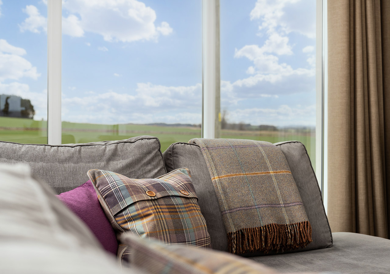 Sofa and cushion detail with a large window with a view behind them in Lodge 1 at Elderburn Lodges in Fife Scotland