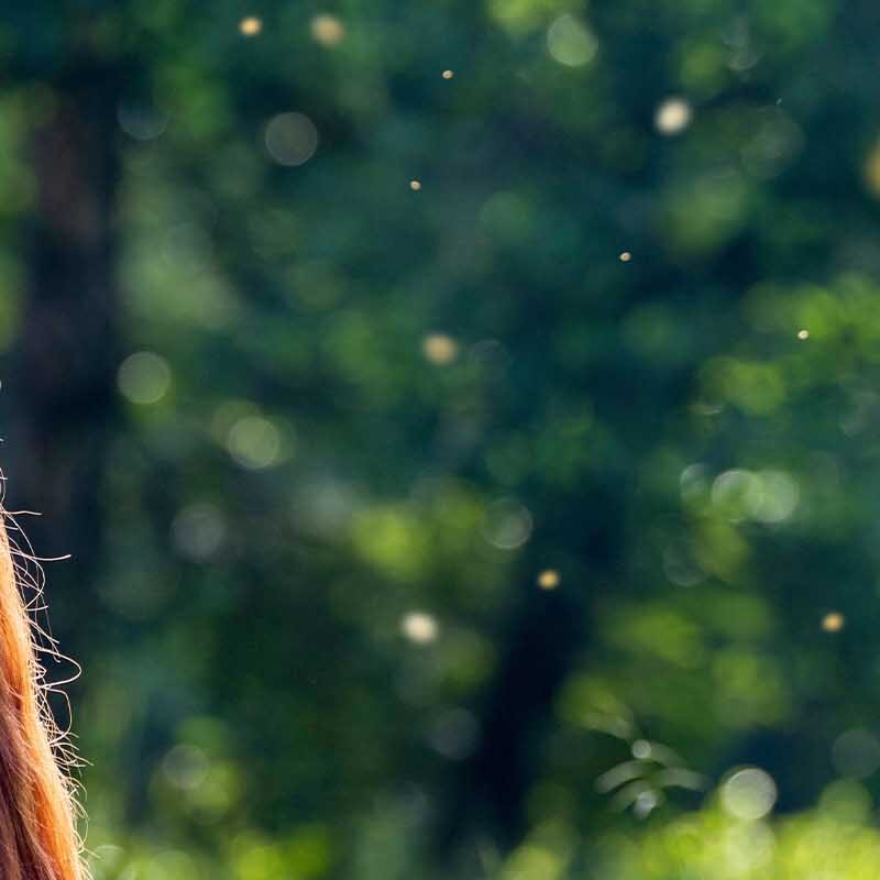 A woman sits outside relaxing as midges fly nearby.